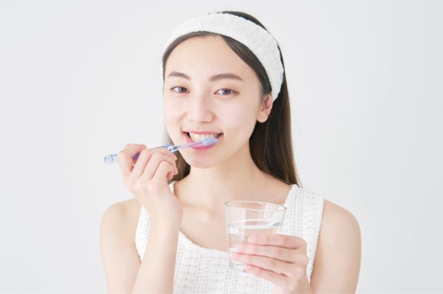 コップを持ちながら歯磨きする女性