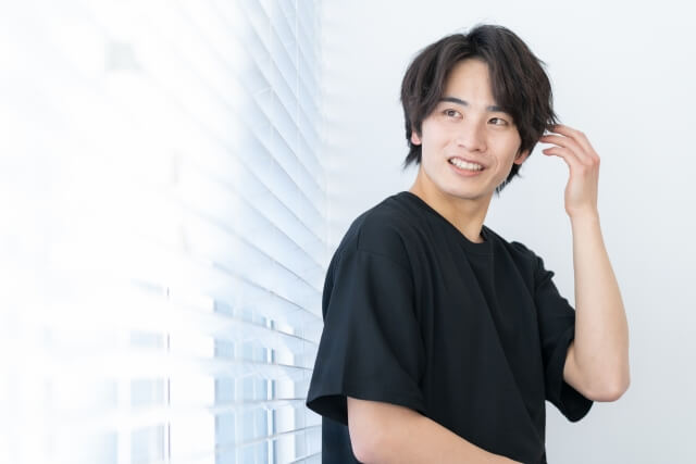 髪を触りながら微笑む若い男性